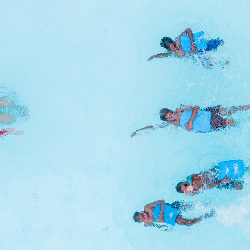 A group of children swim backstroke in a clear blue pool