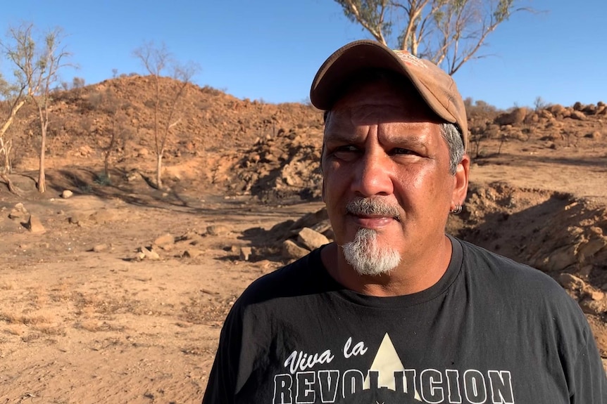 A man, wearing a cap and a black t-shirt, standing outside Alice Springs