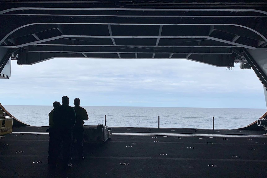 A large open hangar- two people look out over the ocean.