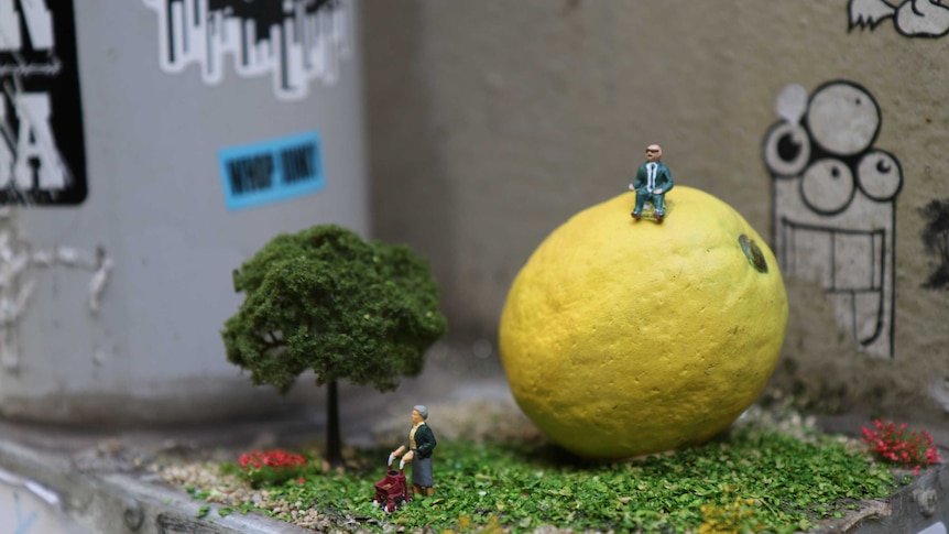 A miniature diorama consisting of a lemon and two elderly figurines