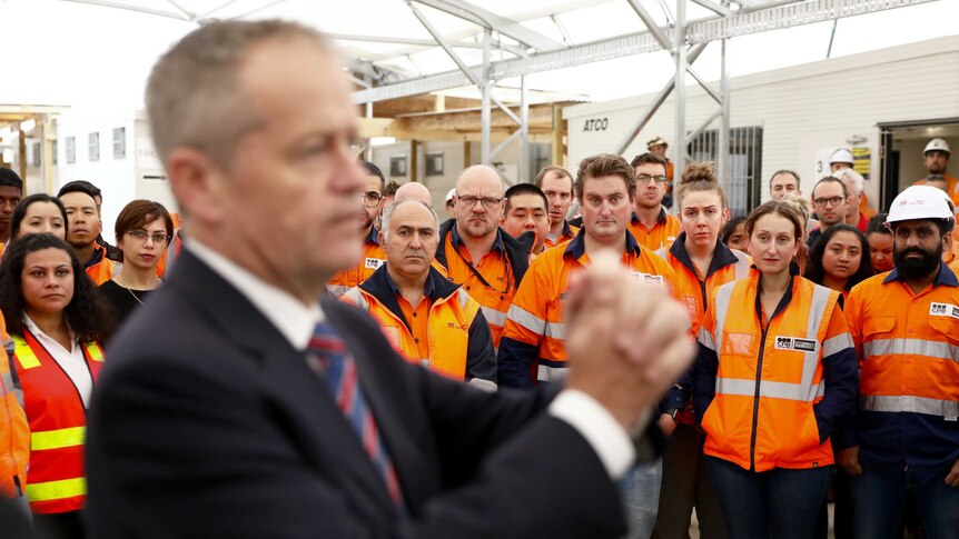 Workers in high-visibility tops listen to Bill Shorten who is speaking to them with his hands clasped