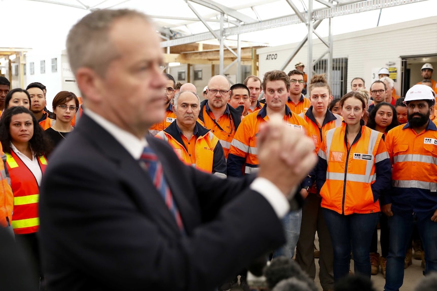 Workers in high-visibility tops listen to Bill Shorten who is speaking to them with his hands clasped