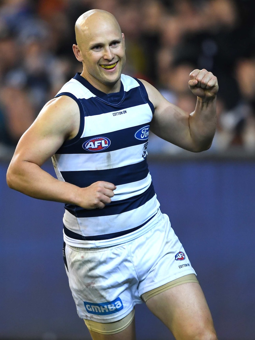 A male AFL player smiles and pumps his left fist as he celebrates kicking a goal.