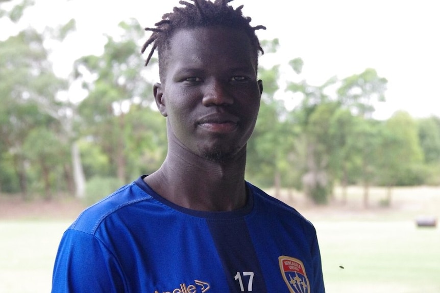 An African man in a sports top looks at the camera with trees in the background