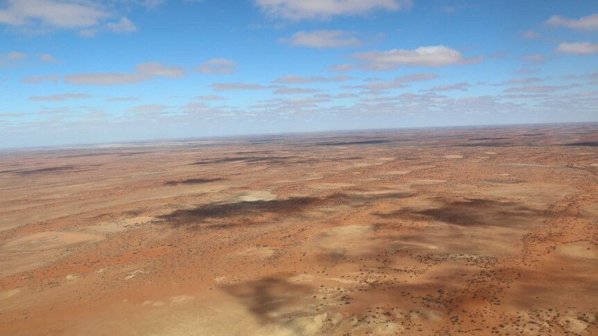 Wide aerial shot of rust-coloured Australian outback below blue sky.