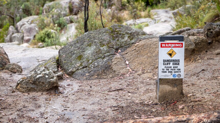 A sign that says dangerous cliffs ahead near a waterfall and rocks. 