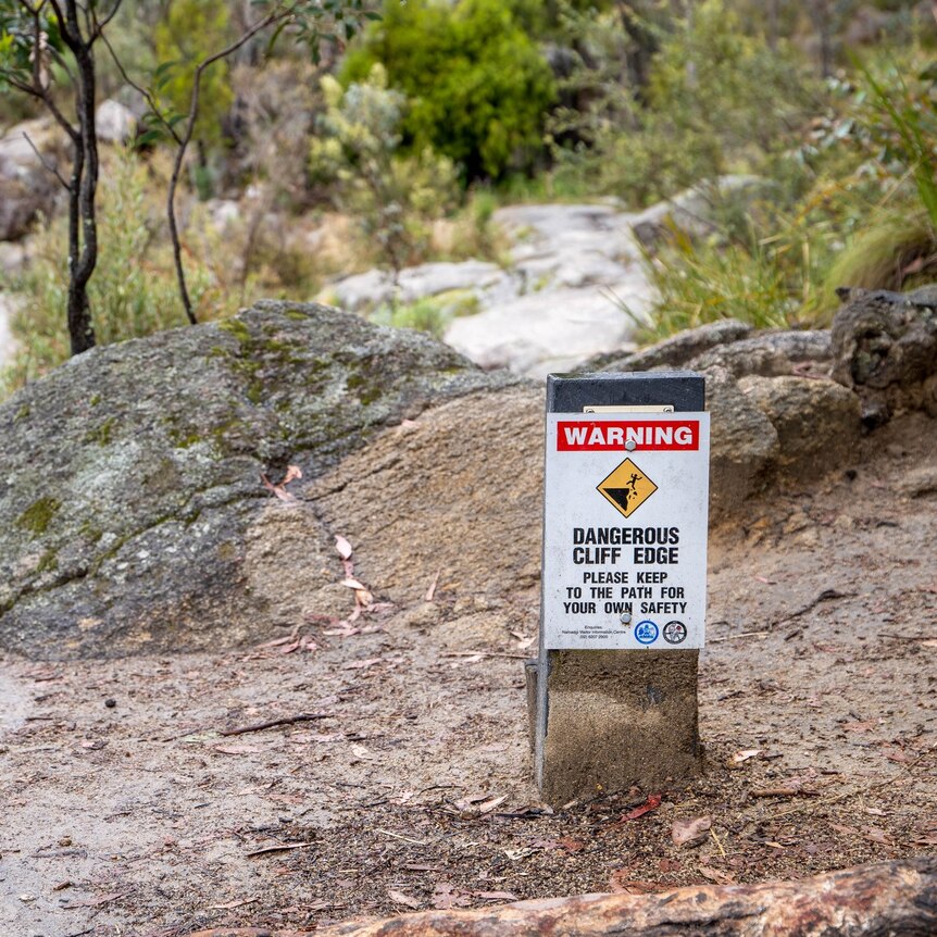 A sign that says dangerous cliffs ahead near a waterfall and rocks. 