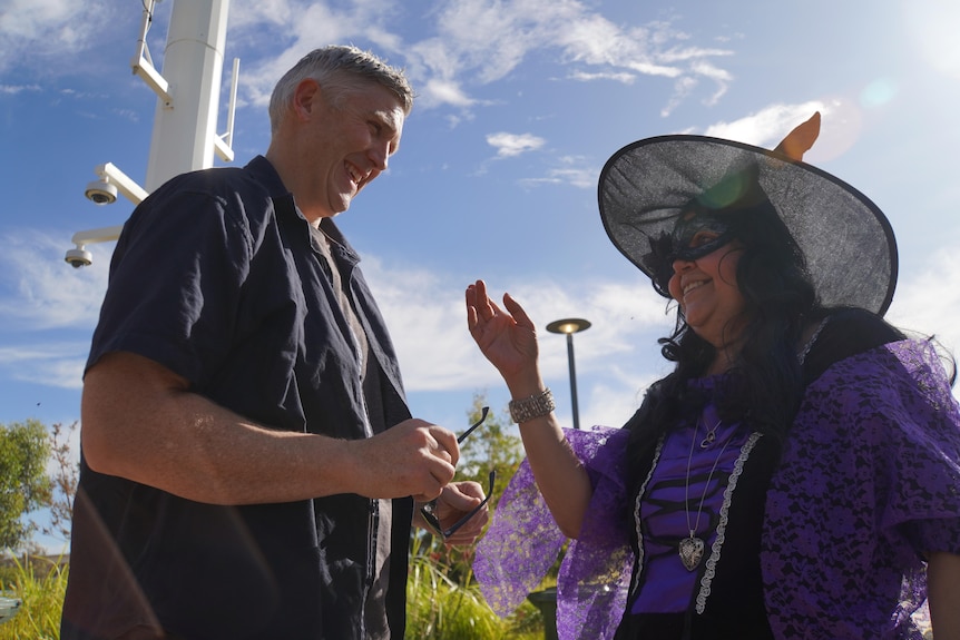 A man smiles while greeting a woman dressed as a witch.