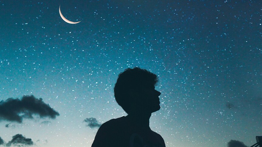 A man silhouetted in darkness looks towards the night sky 