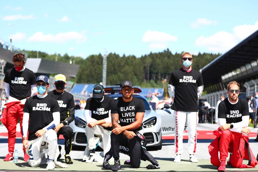 Lewis Hamilton and other drivers take a knee while some drivers stand behind them.