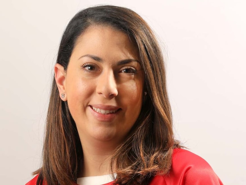 A headshot of Deema Audeh  who wears her long brown hair out with a red shirt as she smiles