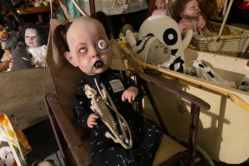 A baby doll with black lips, pig tails and a eye popping out sits in a rustic wheelchair.