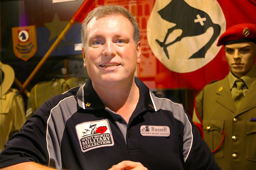 Man smiling in front of flags and military uniform display