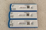 Three small white COVID-19 rapid tests on a benchtop showing positive test results