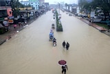 people wade along a street covered in muddy water