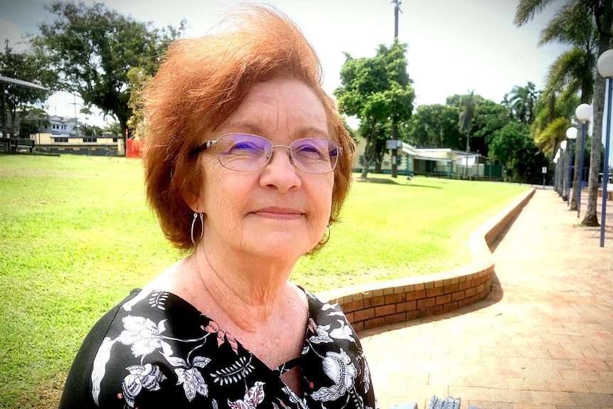 An older woman sitting in a park looks at the camera