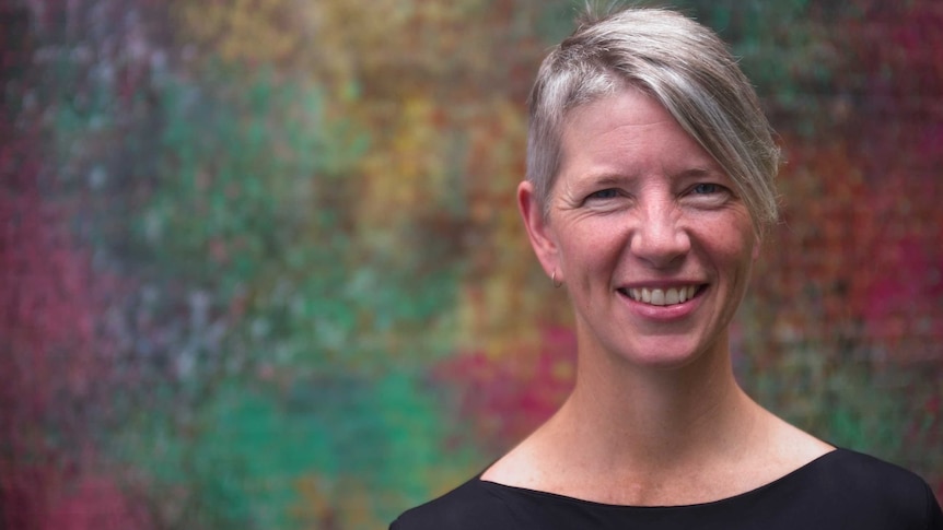 Portrait of woman with short, grey hair against a colourful backdrop.