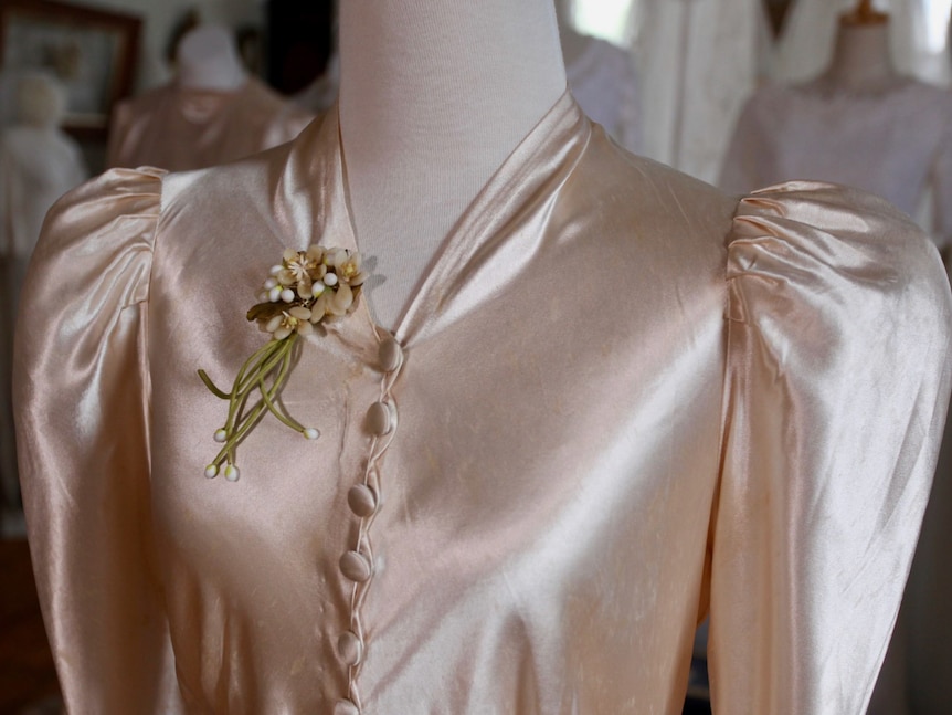 A close-up a ivory wedding dress with mutton sleeves and a row of buttons down the front.
