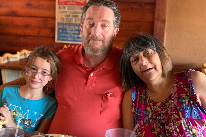 An older man with his arms wrapped around a nine-year-old girl and an older woman