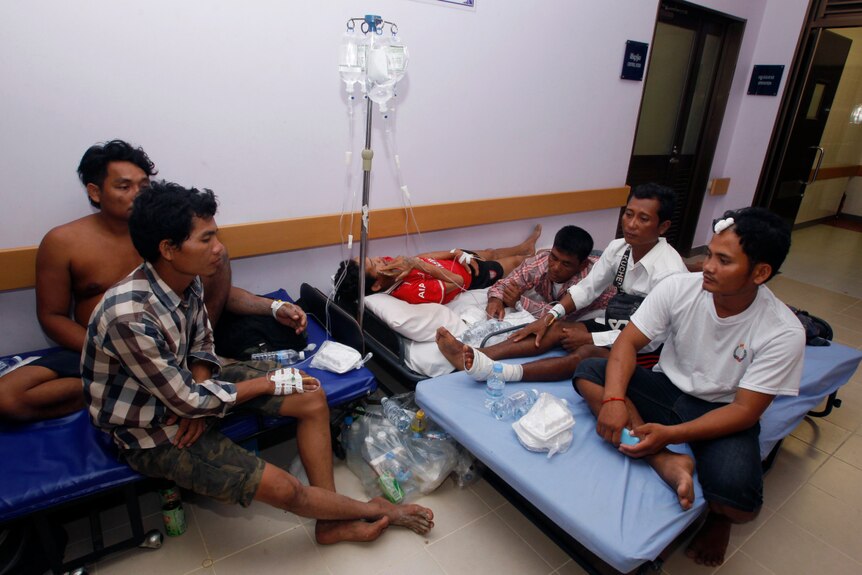 A group of injured men sit on blue hospital mattresses in a corridor.