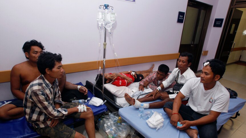 A group of injured men sit on blue hospital mattresses in a corridor.