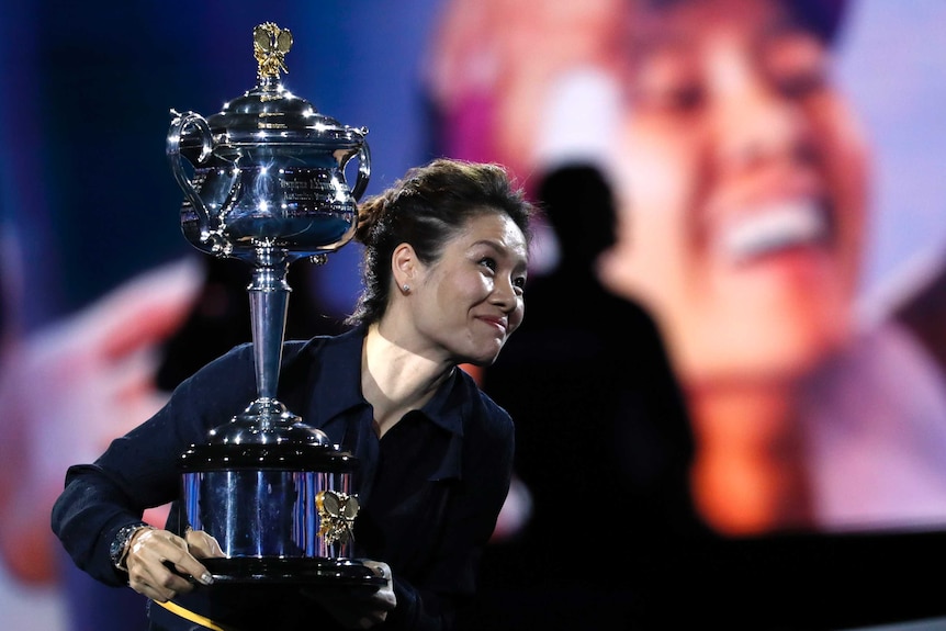 You view Li Na with a very shallow depth of field with her hands surrounding a large silver trophy.