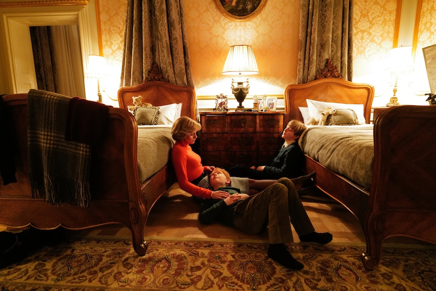 A young boy lies in a 30-something blonde woman's lap, with another sitting across from them against the side of a bed