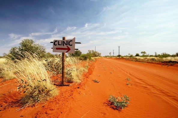 A handpainted sign reading clinic points the way on an orange desert track in remote Central Australia