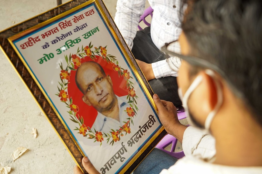 A young man holding a framed photo of an older man