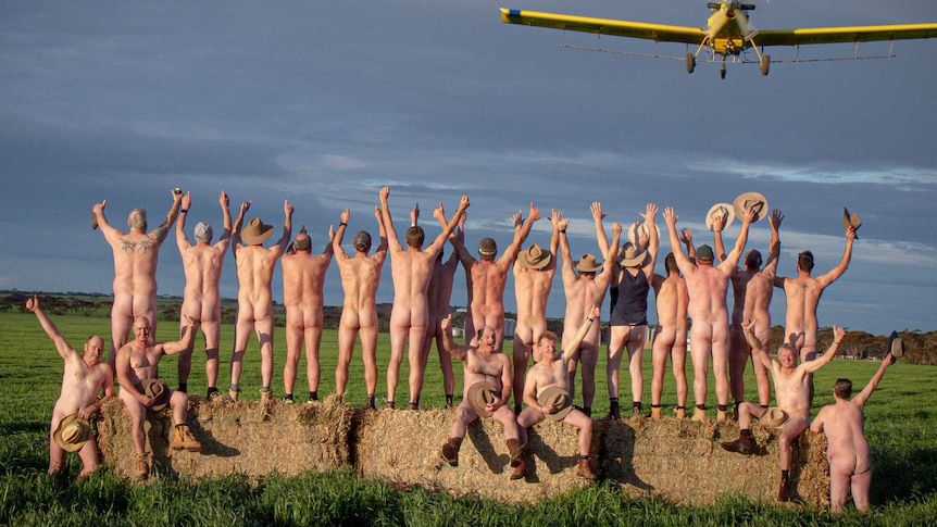 A small plane flies over a group of 21 naked men who have their bums facing towards the camera.