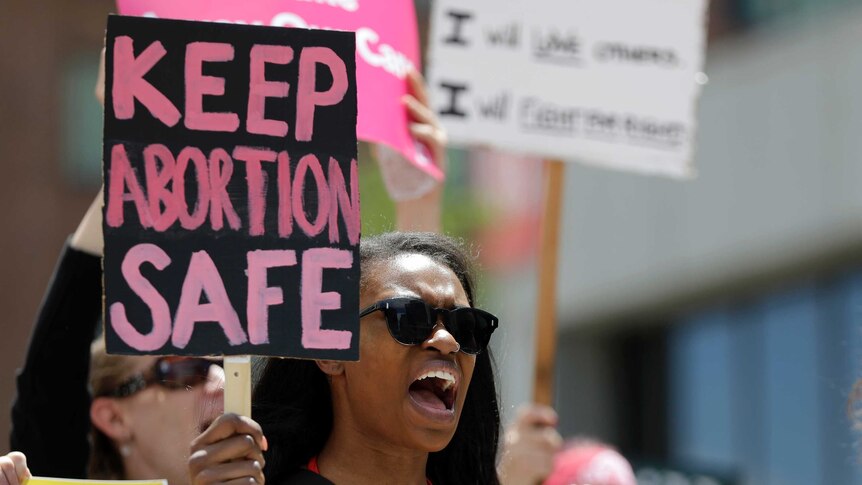 A woman wearing sunglasses marches and holds a sign promoting women's abortion rights
