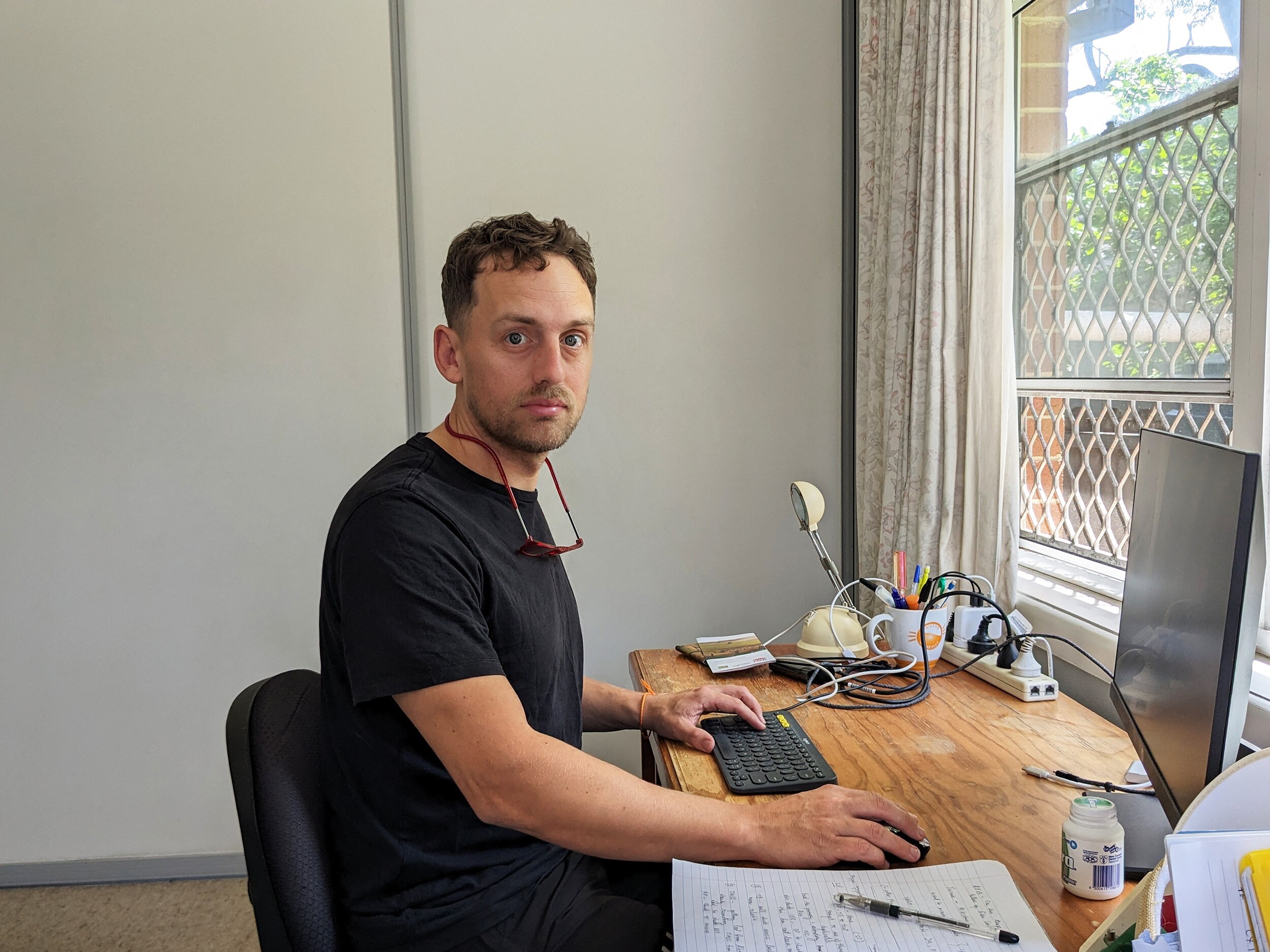 Kurt sits at his desk in front of his laptop and looks at the camera