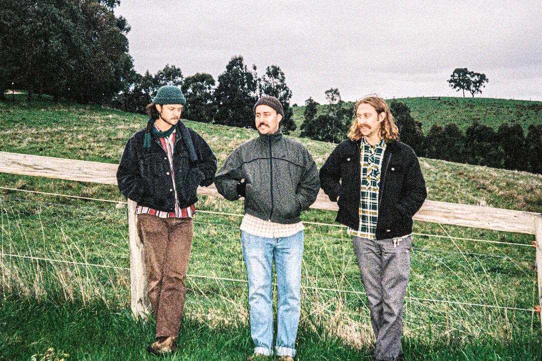 A grainy film photo of three men in jackets and jeans in a paddock.