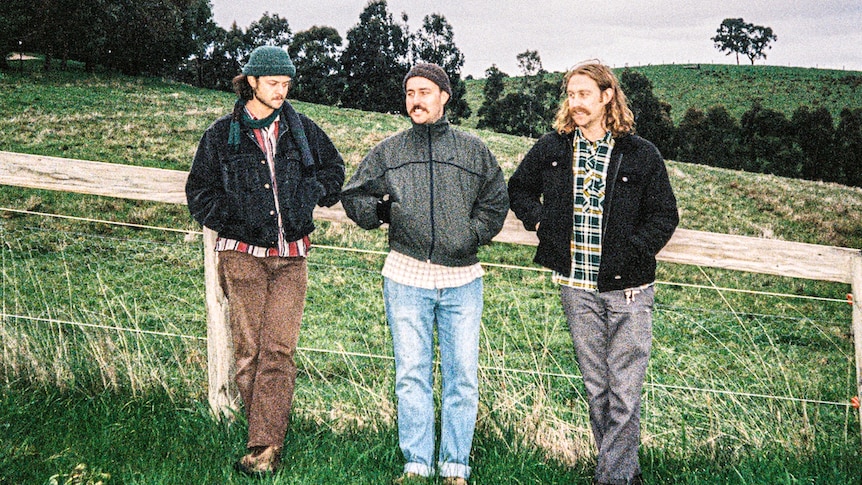 A grainy film photo of three men in jackets and jeans in a paddock.