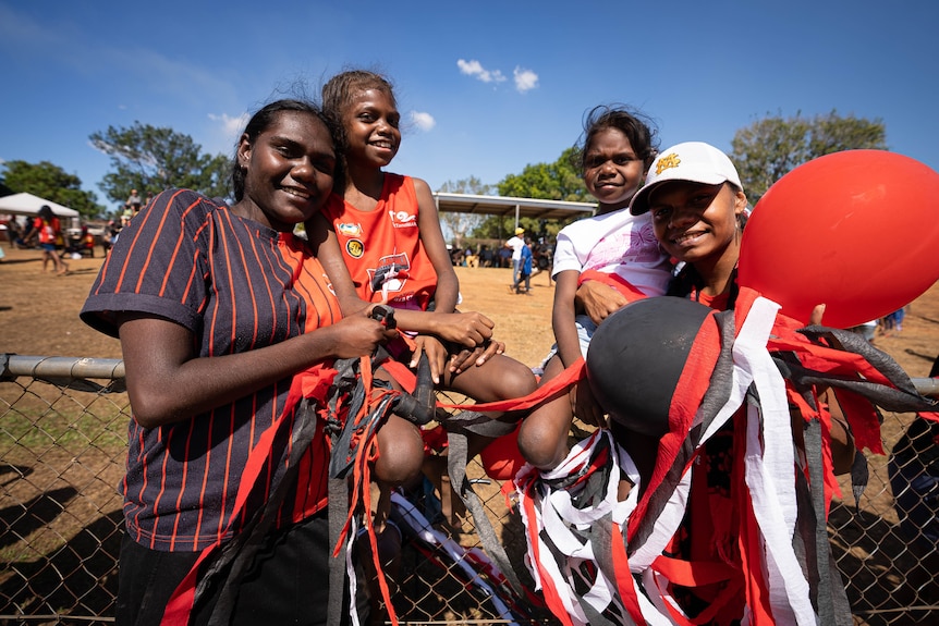 A group of four football fans gathered on the sidelines of an oval.