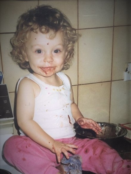 Amy White as a baby, playing with food on a bench top.