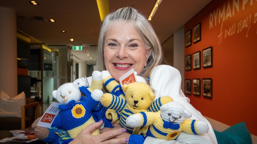 A woman smiles as she holds hand-knitted teddy bears in her arms.