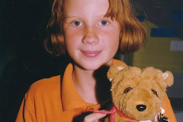 A smiling red-haired child holding a toy in a school uniform