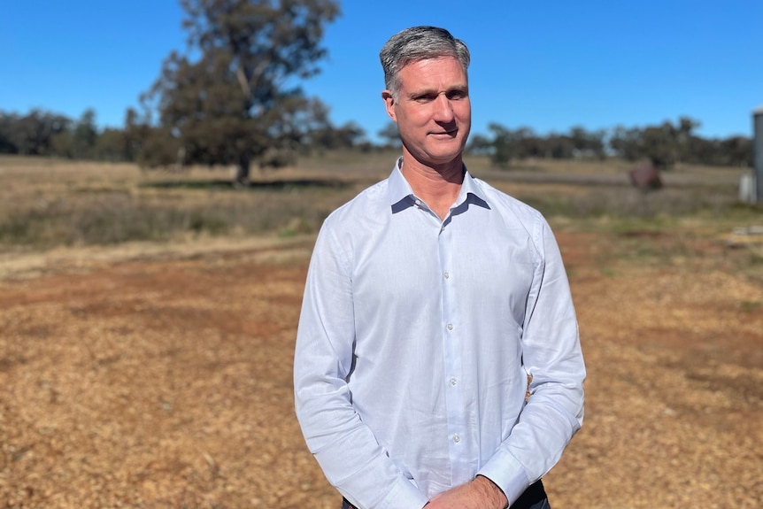 A tall man with short grey hair standing in a dusty paddock.