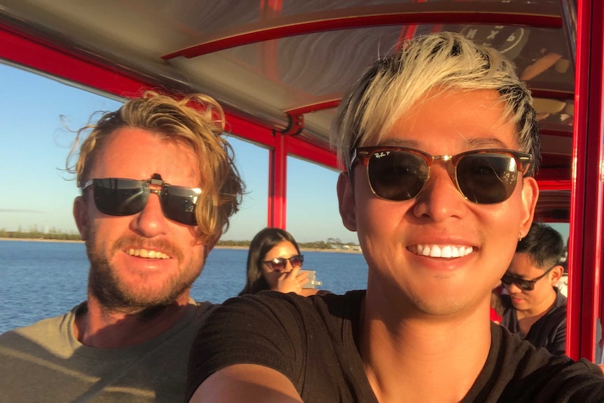 Two young men wearing sunglasses smile to the camera while in a red carriage, the water and beach behind them.