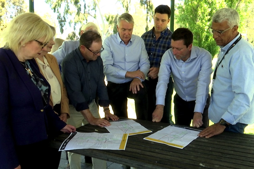 A group of people in business attire stand around a table looking at an infrastructure plan.