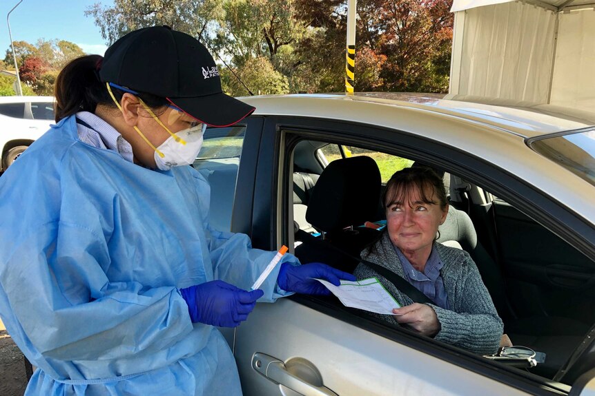 A woman in a car prepares to be tested for coronavirus by a nurse.