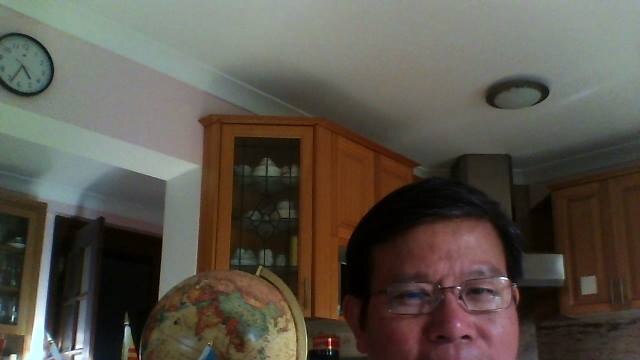 Chau Van Kham sitting in a living room next to a globe with an Australian flag and Viet Tan flag.