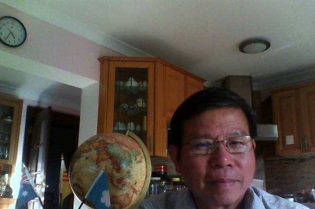 Chau Van Kham sitting in a living room next to a globe with an Australian flag and Viet Tan flag.