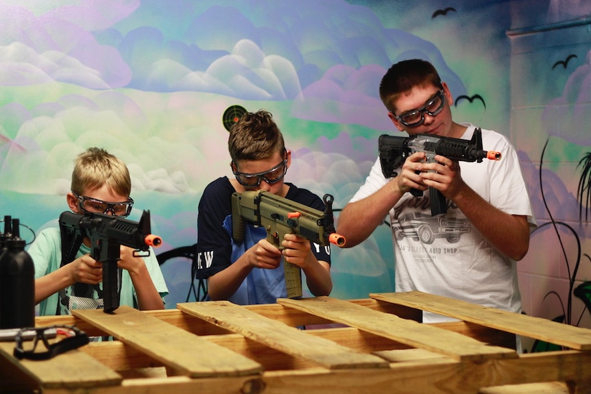 Three children wearing protective goggles take aim with gel ball blasters during a skirmish-style game in Brisbane.
