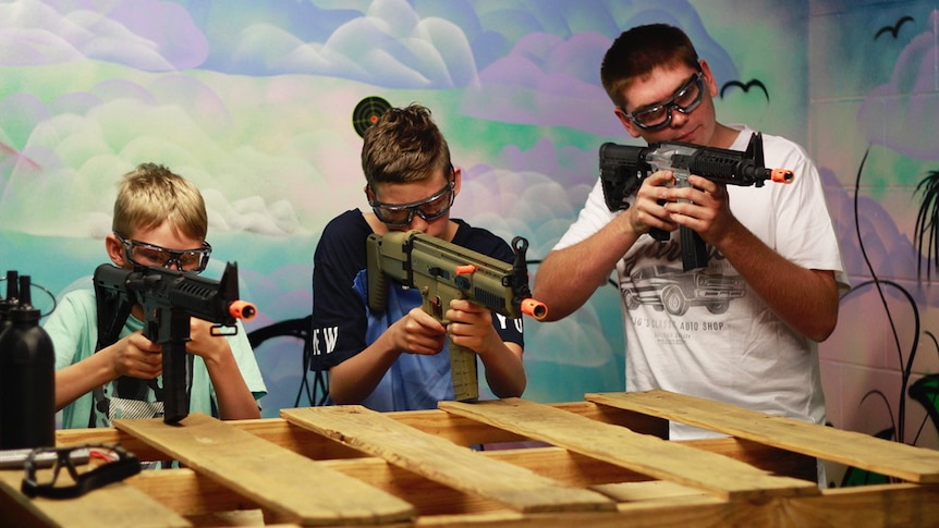 Three children wearing protective goggles take aim with gel ball blasters during a skirmish-style game in Brisbane.