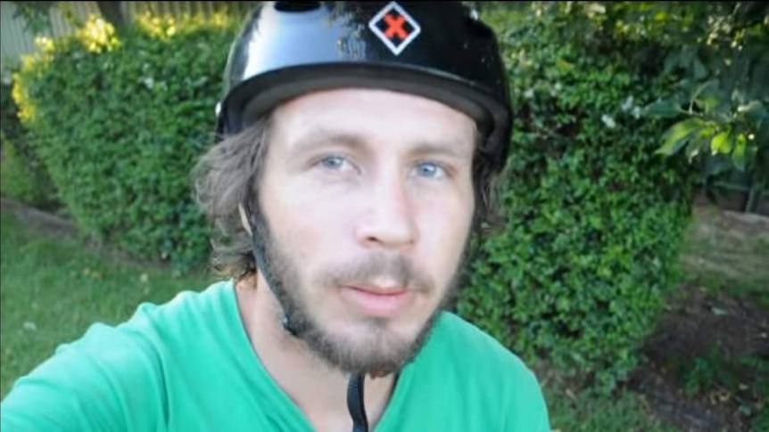 A man with a beard, wearing a black bike helmet and a green t-shirt, looks at the camera.