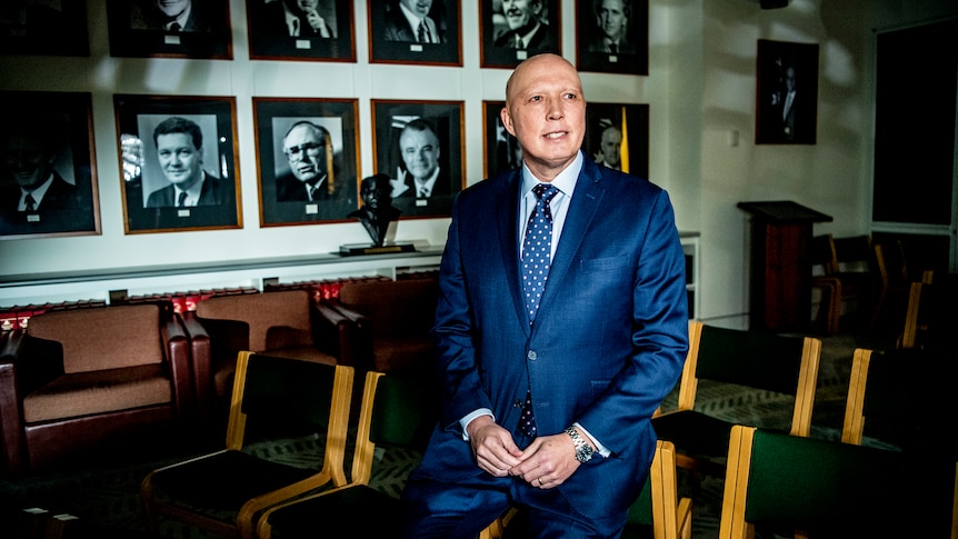 Peter Dutton sits on a chair with portraits of former Liberal leaders behind him.