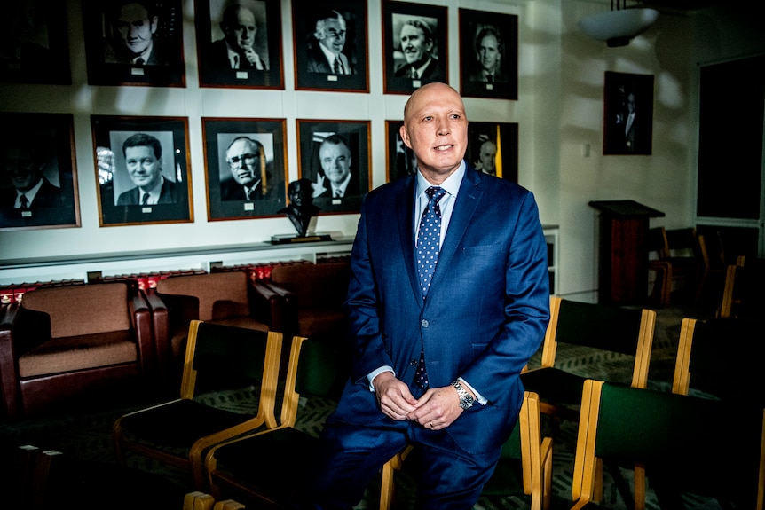 Peter Dutton sits on a chair with portraits of former Liberal leaders behind him.