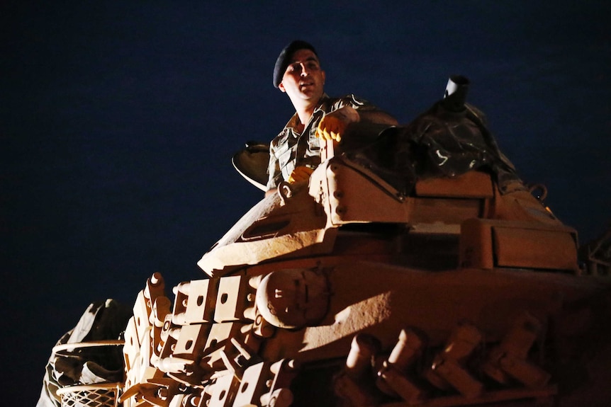 A Turkish army officer sits atop this tank at night.